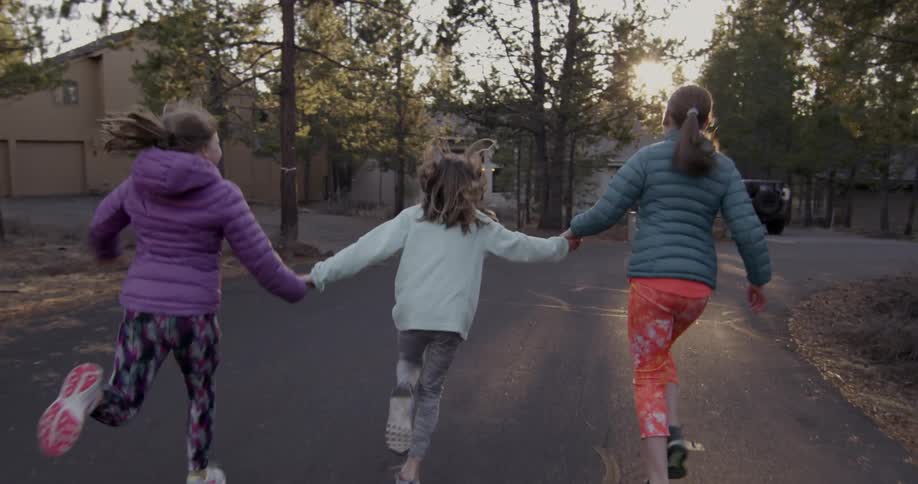 Three girls hold hands and run in a residential area