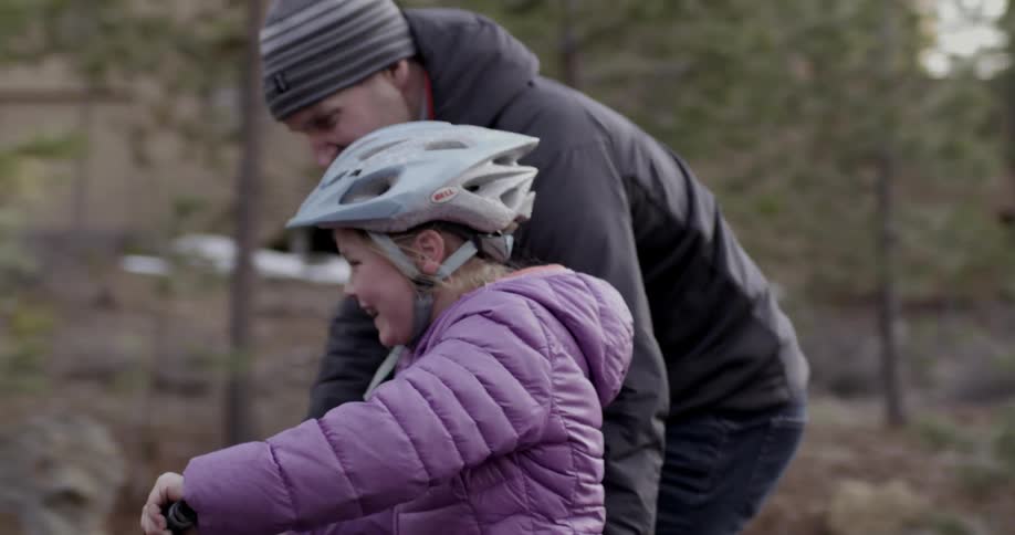 A little girl is helped by her father as she tries to ride a bicycle