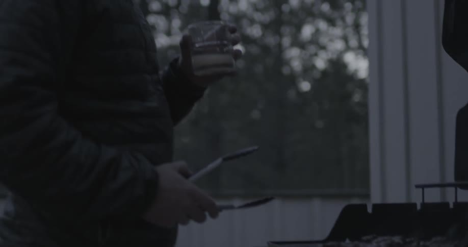 Man grills meat and takes a sip of his drink