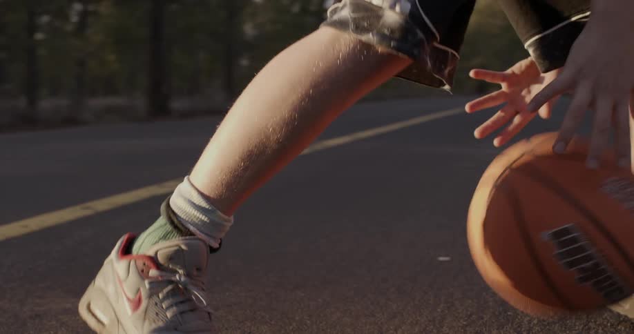 A boy is dribbling a basketball between his legs