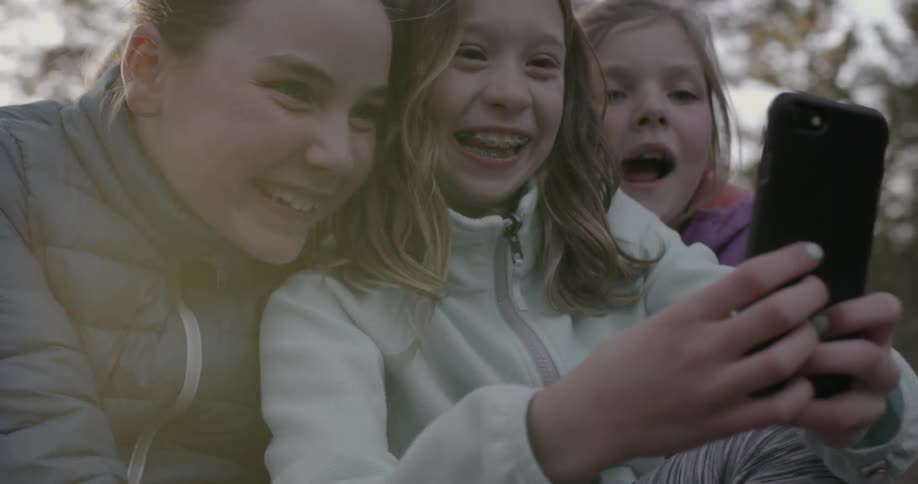 Three young girls taking a selfie outdoors on a chilly day