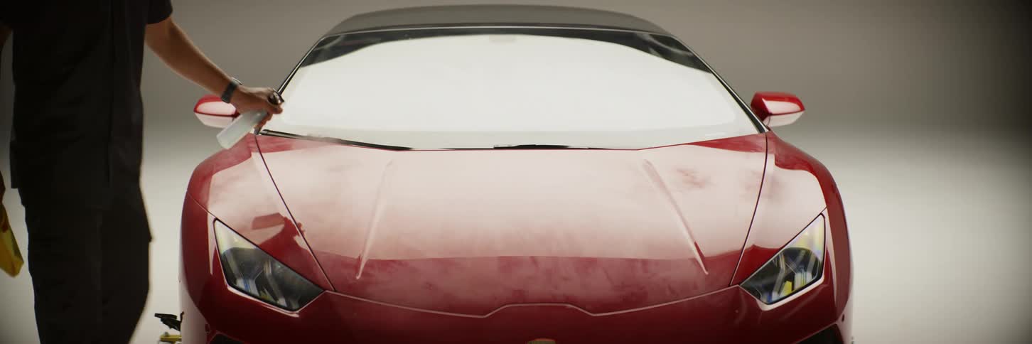 A man sprays water on the bodywork of a red sports car