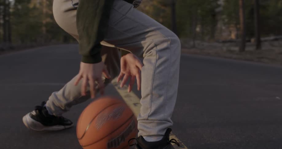 A man dribbles a basketball through his legs on the blacktop