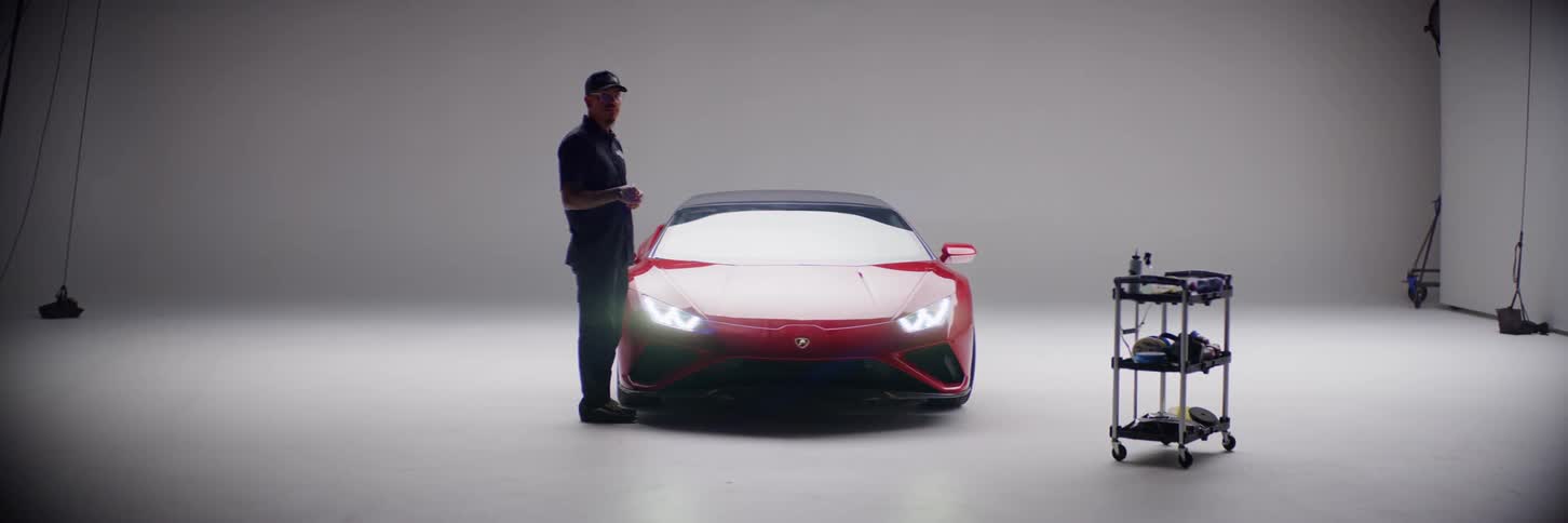 A man is standing next to a red sports car that is parked in a photo studio with a white background