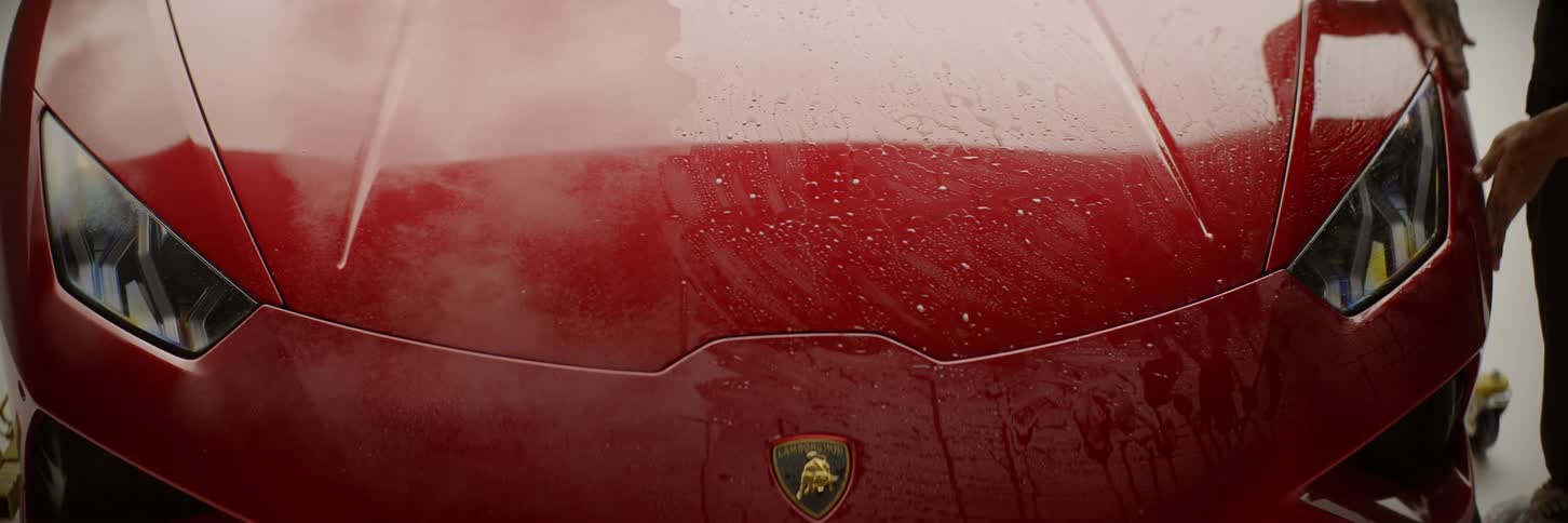 Man washing the headlights of a red lamborghini with his hands