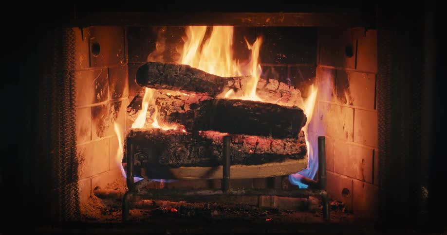 Stack of logs burning in a fireplace at night creating an orange glow