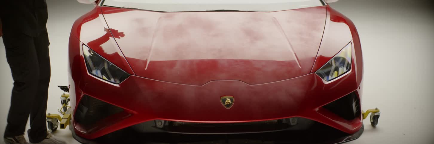 A man sprays liquid onto the hood of a red luxury car