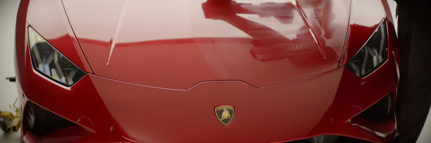 A man uses a machine to polish the hood of a red luxury car