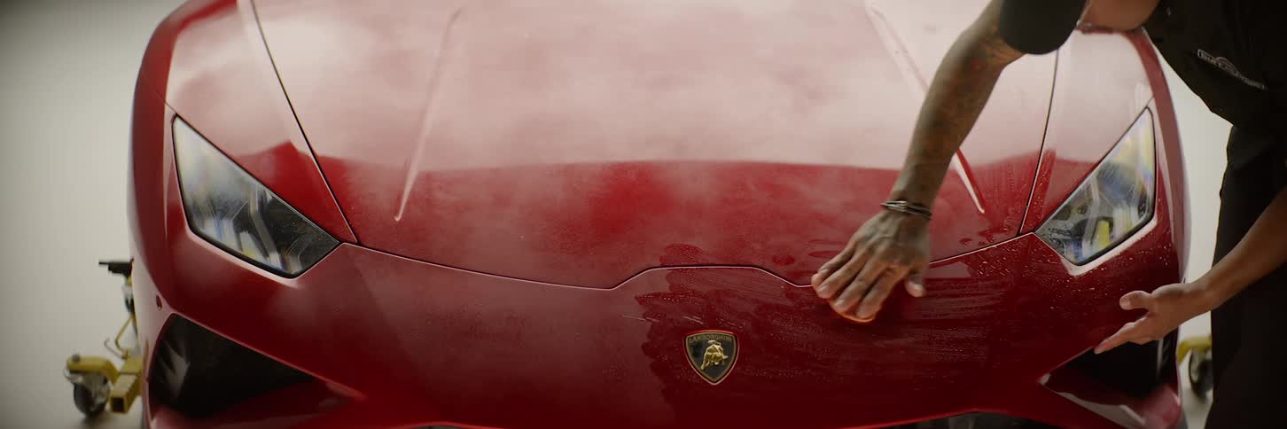 A man is polishing the front bodywork of a red sports car