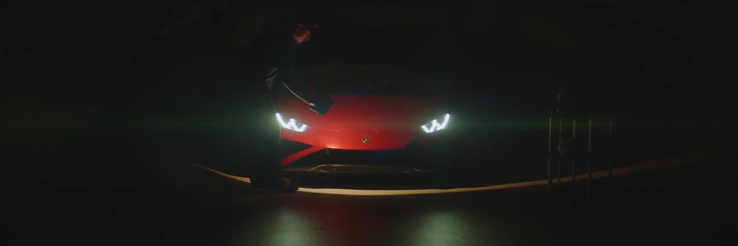 Dark room with a red lamborghini headlights on and a man with a flashlight passing by