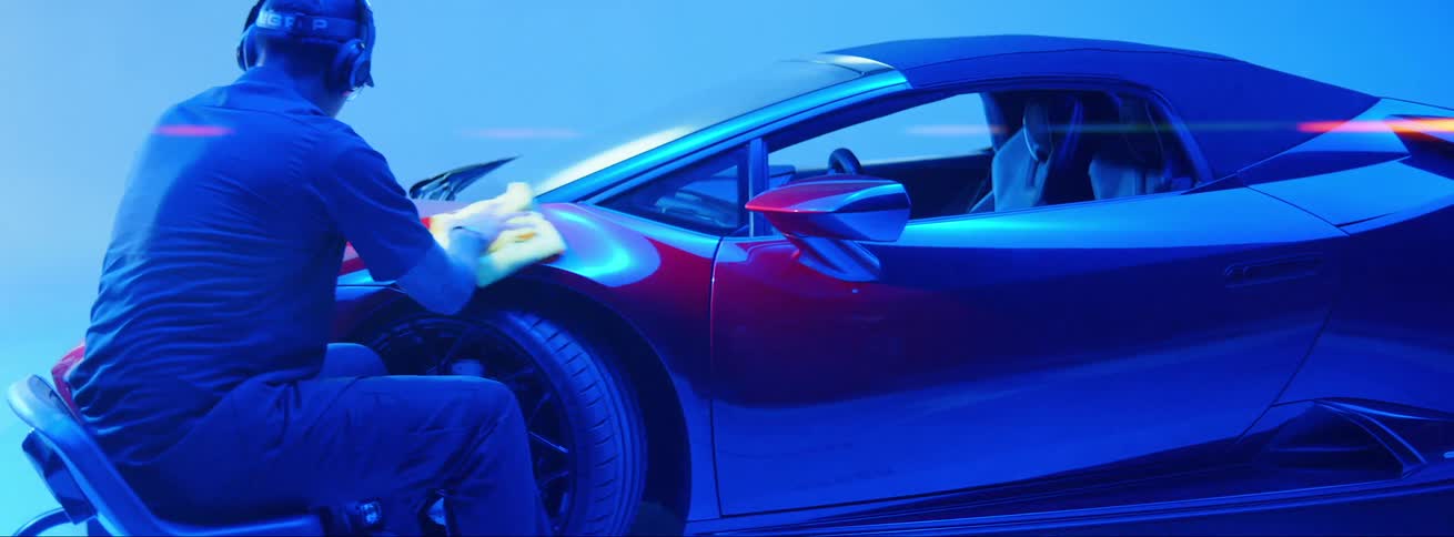 A man sitting down is cleaning a car and the part he cleans is blue and is turning red