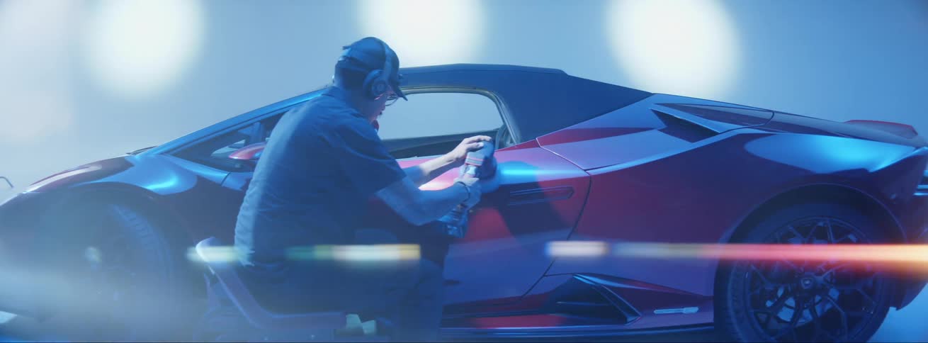 A man is using a machine to polish the door of a red luxury car