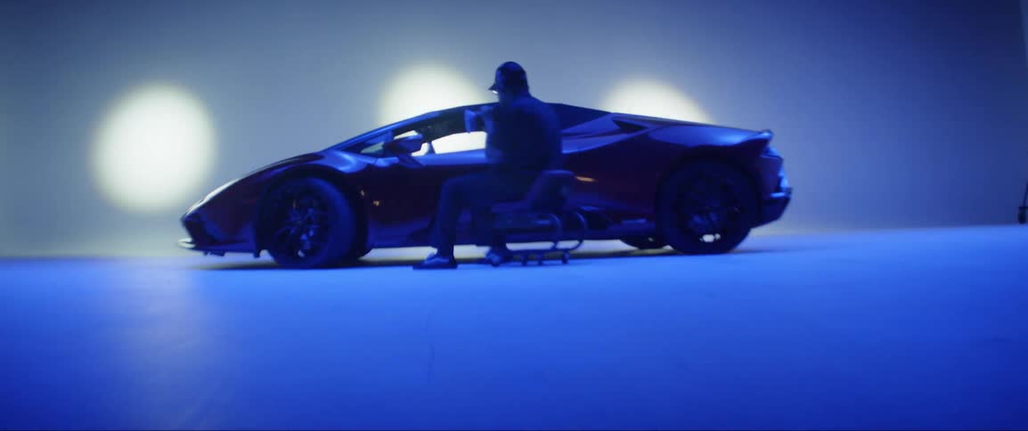 Man sitting in a chair facing a red lamborghini inside a studio
