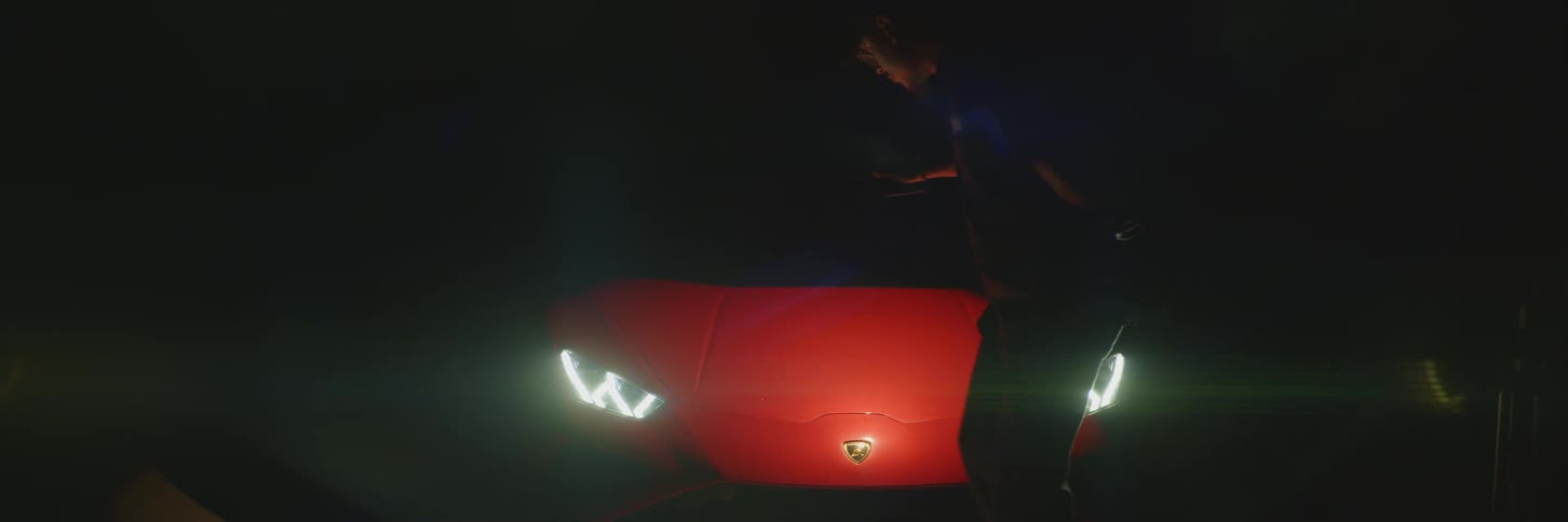 View of a man with a flashlight checking inside the dark interior of a red lamborghini with the headlights on