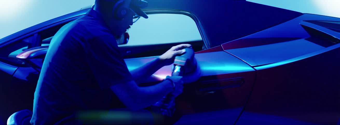 Man sitting in a chair polishing the side door of a red lamborghini inside a studio