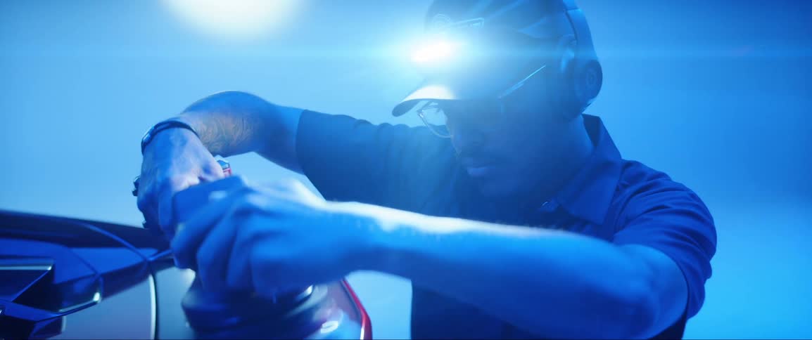 A man with a flashlight on his hat is polishing a car with a tool and the entire environment has blue lights