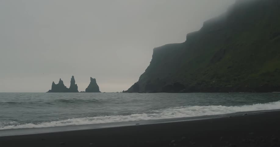 A beach with small waves breaking on the shore and in the water there are some sharp rocks that come out to the surface