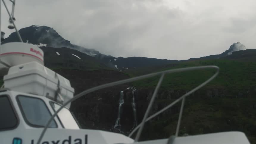 A white boat and in the background a huge mountain and the sky is all cloudy