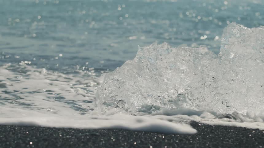 Closeup of a wave at the edge of black sand with ice