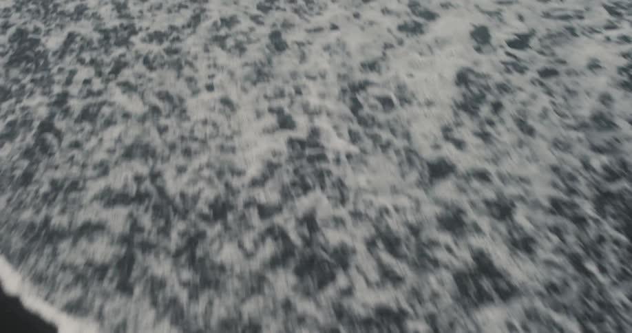Small waves arriving on the shore of a beach with dark sand