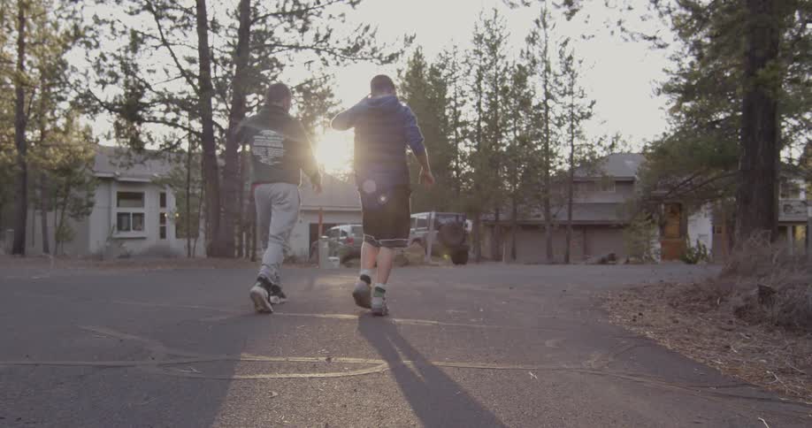 Two boys walk down a street lined with houses and trees