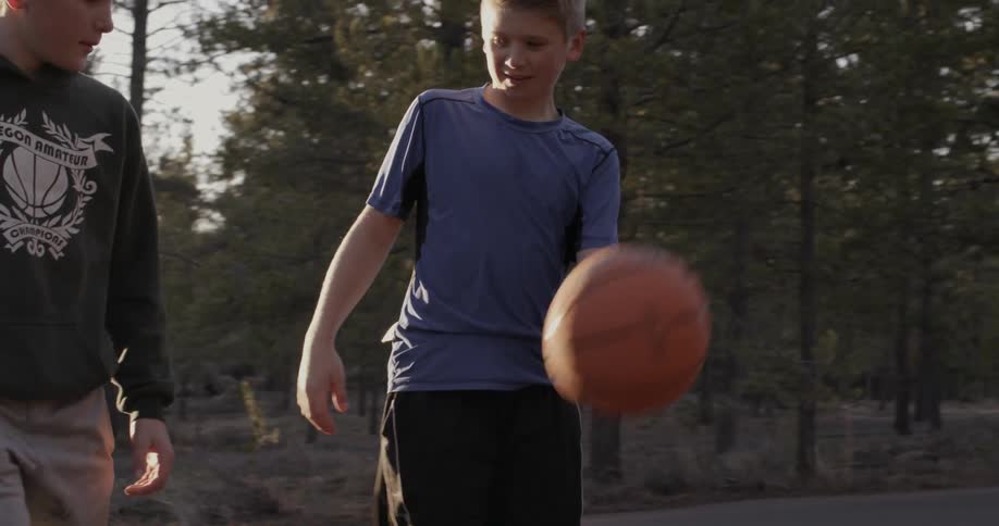 A two boys with a basketball are crossing a rural road