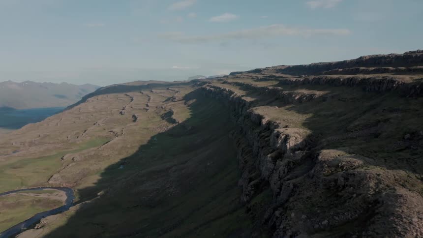 An aerial view of a region with a huge hill and mountains and the sea on the left
