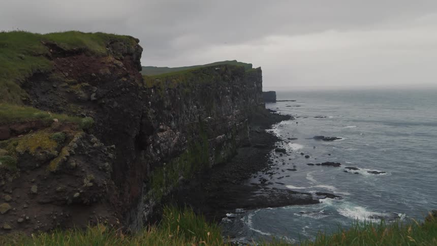 A sea coast with a huge high gorge and some birds flying over the sky