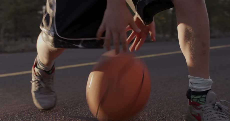 A man dribbles a basketball through his legs on the blacktop