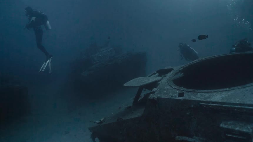 Two divers in the midst of the blue sea with tanks at the bottom of the ocean