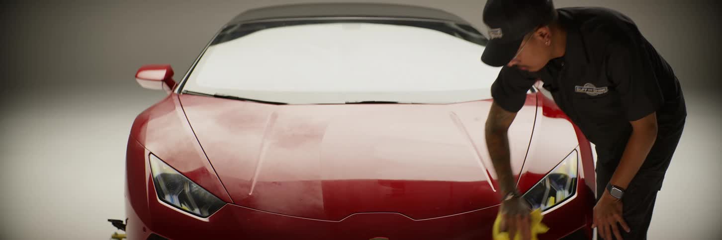 Man wiping the hood of a red lamborghini with a cloth