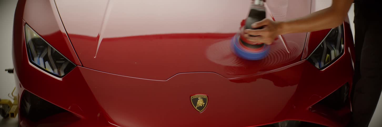 Closeup of the front of a red lamborghini with a person polishing it