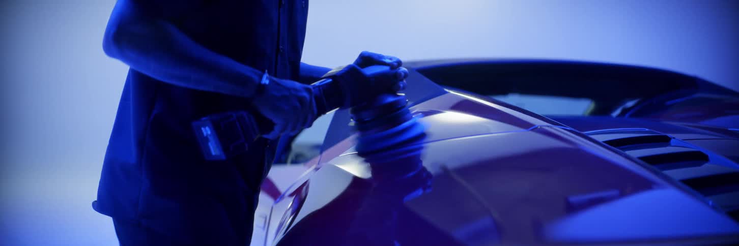 A man is polishing the bodywork of a sports car and the room is lit with strong blue lights