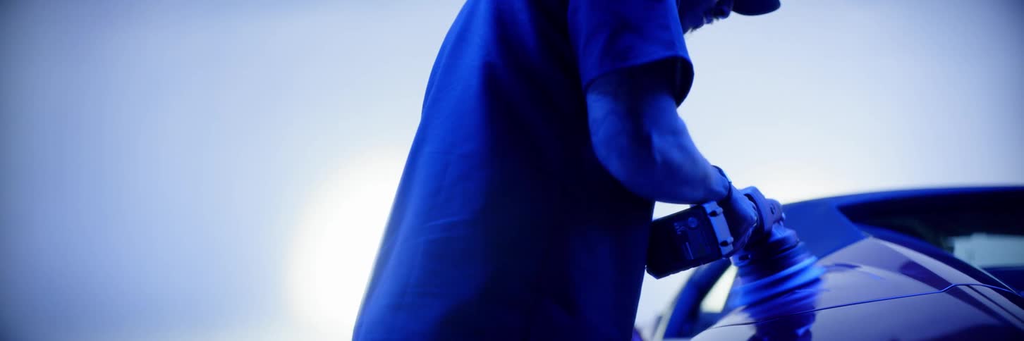 A man is polluting the bodywork of a sports car and the room is lit with strong blue lights
