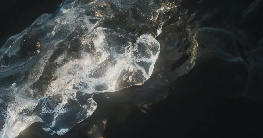 Closeup of ice amidst black sand with seawater