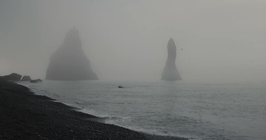 Panorama of a beach with black sand and rocky peaks in the sea on a sunny day
