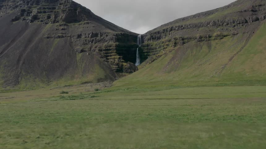 Panorama of a grassland with mountains and a waterfall on a cloudy day