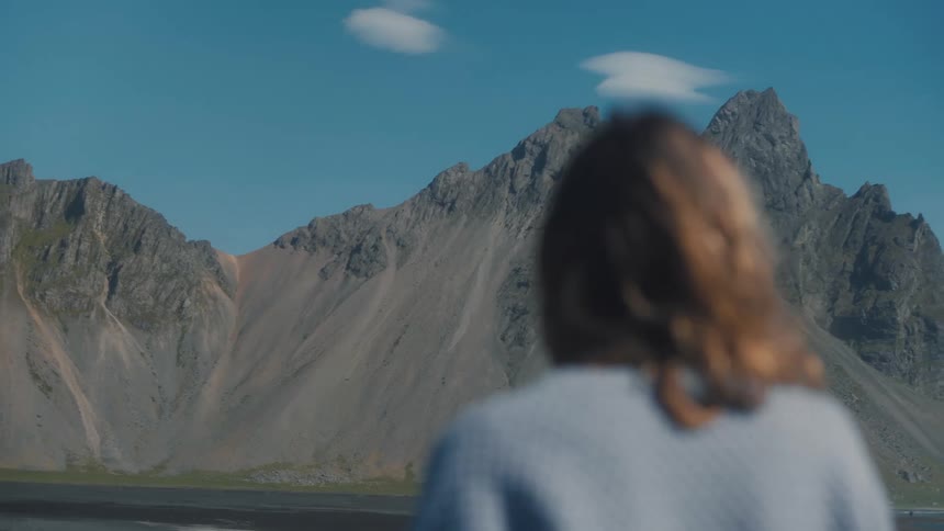 Woman walking in a natural setting in front of a mountain range and cliffs on a day with a blue sky