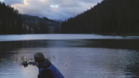 A boy throws a rock into a lake surrounded by hills
