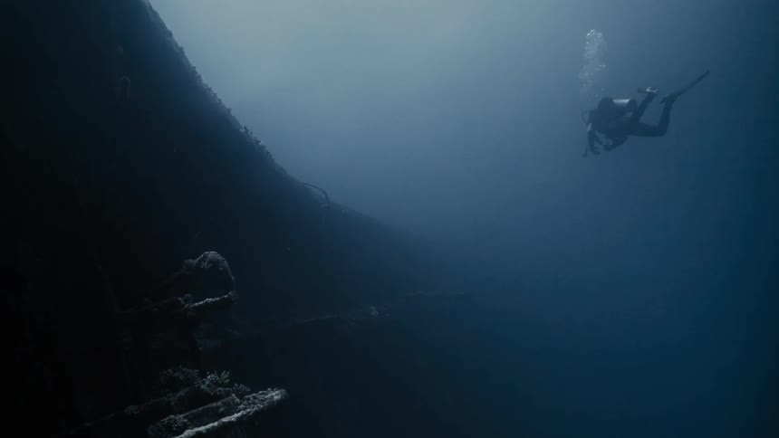 A diver at the bottom of the ocean observing a sunken ship