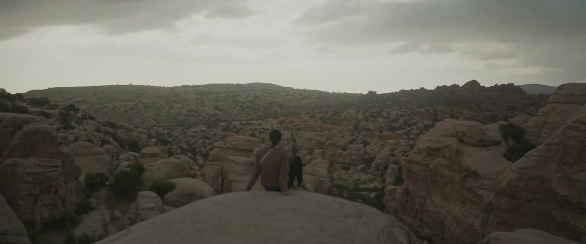 A woman sitting on a rock facing a view amidst rocks and valleys under a morning sky