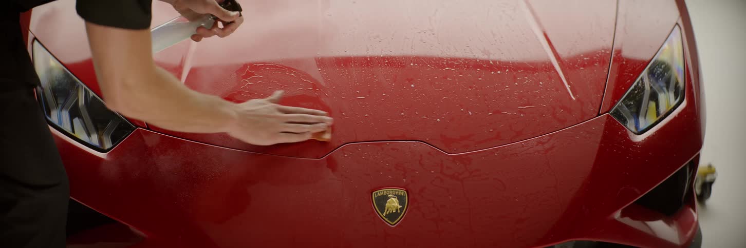 A man is using a cloth to polish the front bodywork of a red sports car