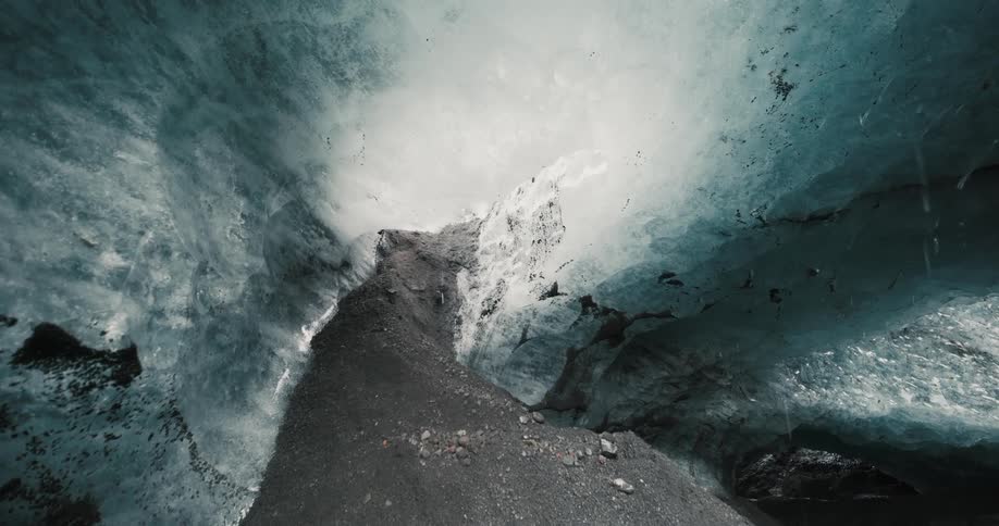 Water dropplets falling into a glacial cave from a thin sunlit sheet of ice above