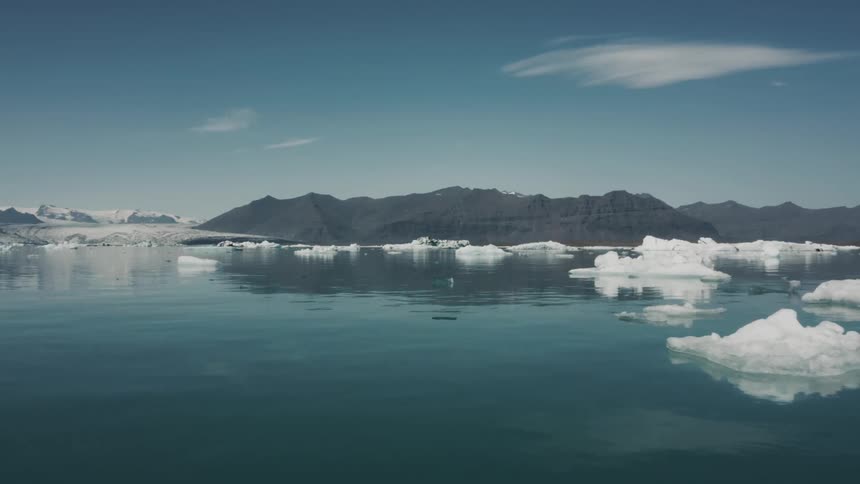Blocks of arctic ice float in the ocean with a mountain range in the distance