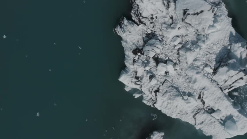 Aerial view straight down over a glacial rock surrounded by dark water
