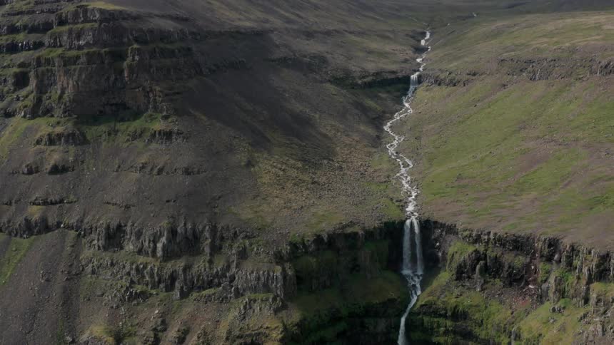Aerial of river through moss covered rock flowing into a waterfall over a canyon during the day