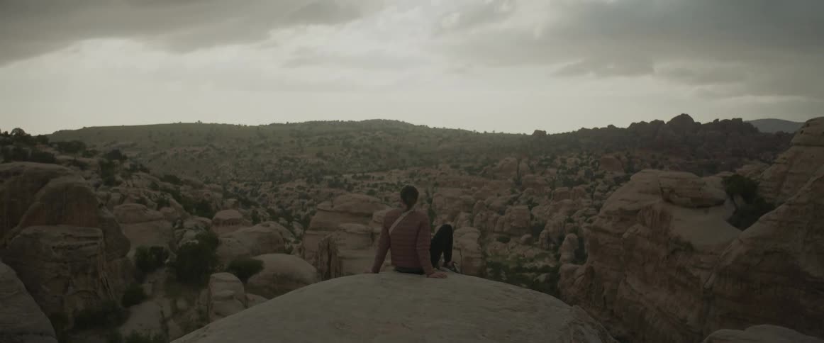 Person sitting with a panoramic view of rocky valleys on a cloudy day