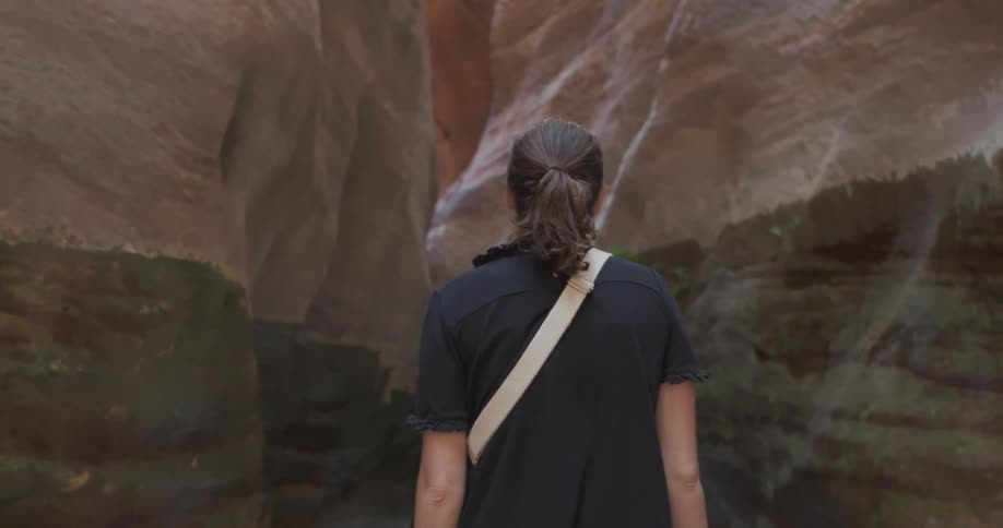 Woman walking away back facing the camera amidst the ruins of a valley