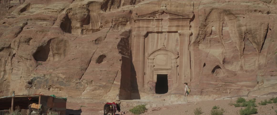 An ancient architecture carved into the wall with a door and a woman passes by