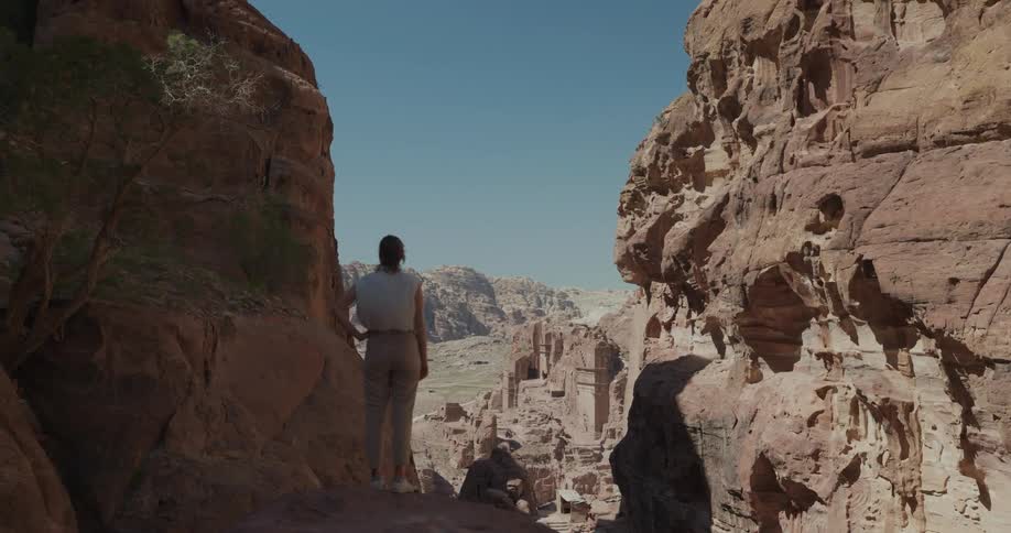 View of a woman with her back to the camera standing on a rock with a panoramic landscape of canyons during the day